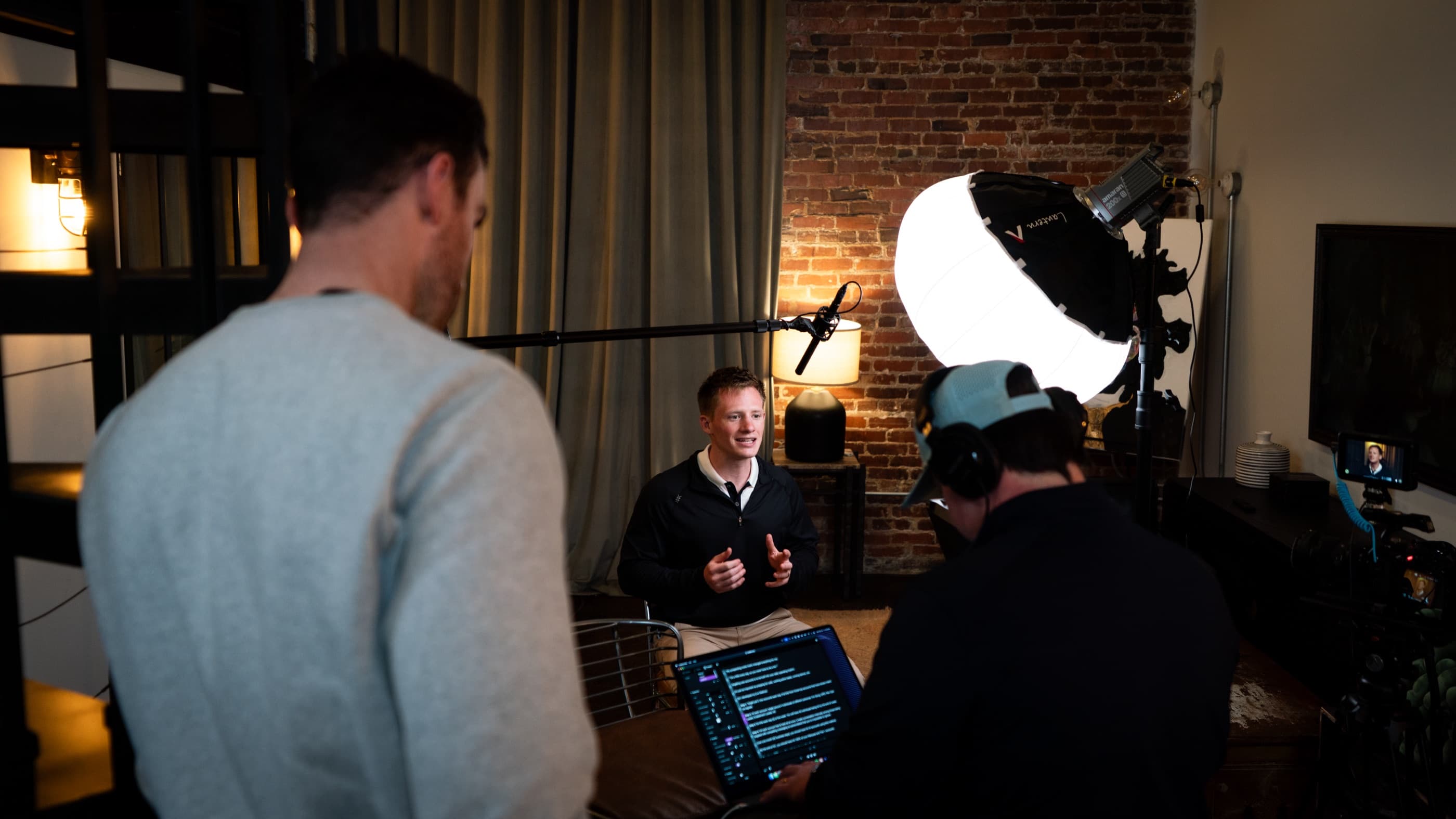 Brian LaManna talking to camera against an exposed brick wall, boom mic overhead and the crew watching from a laptop in the foreground.