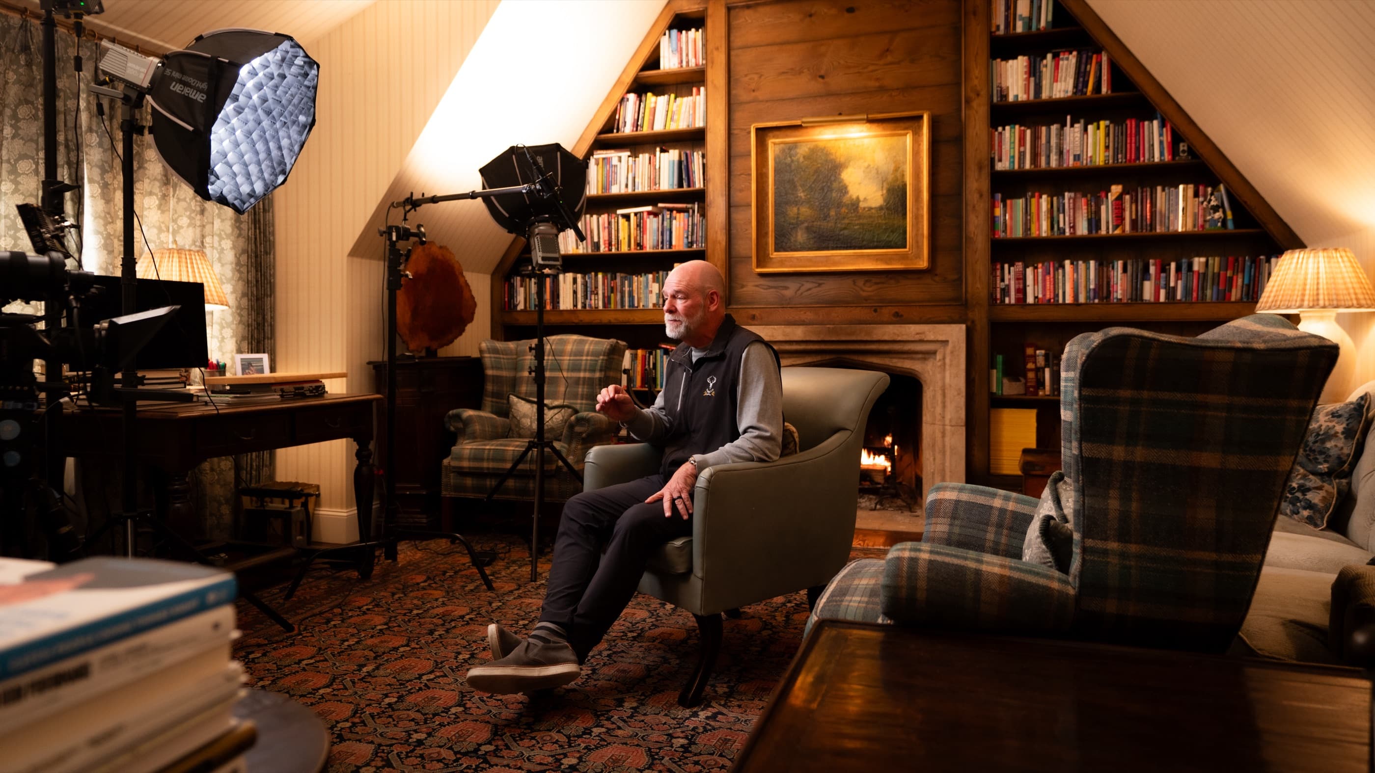 Mark Miller seated for an interview in a panelled attic library, a fire lit behind him and two softboxes rigged to camera left.