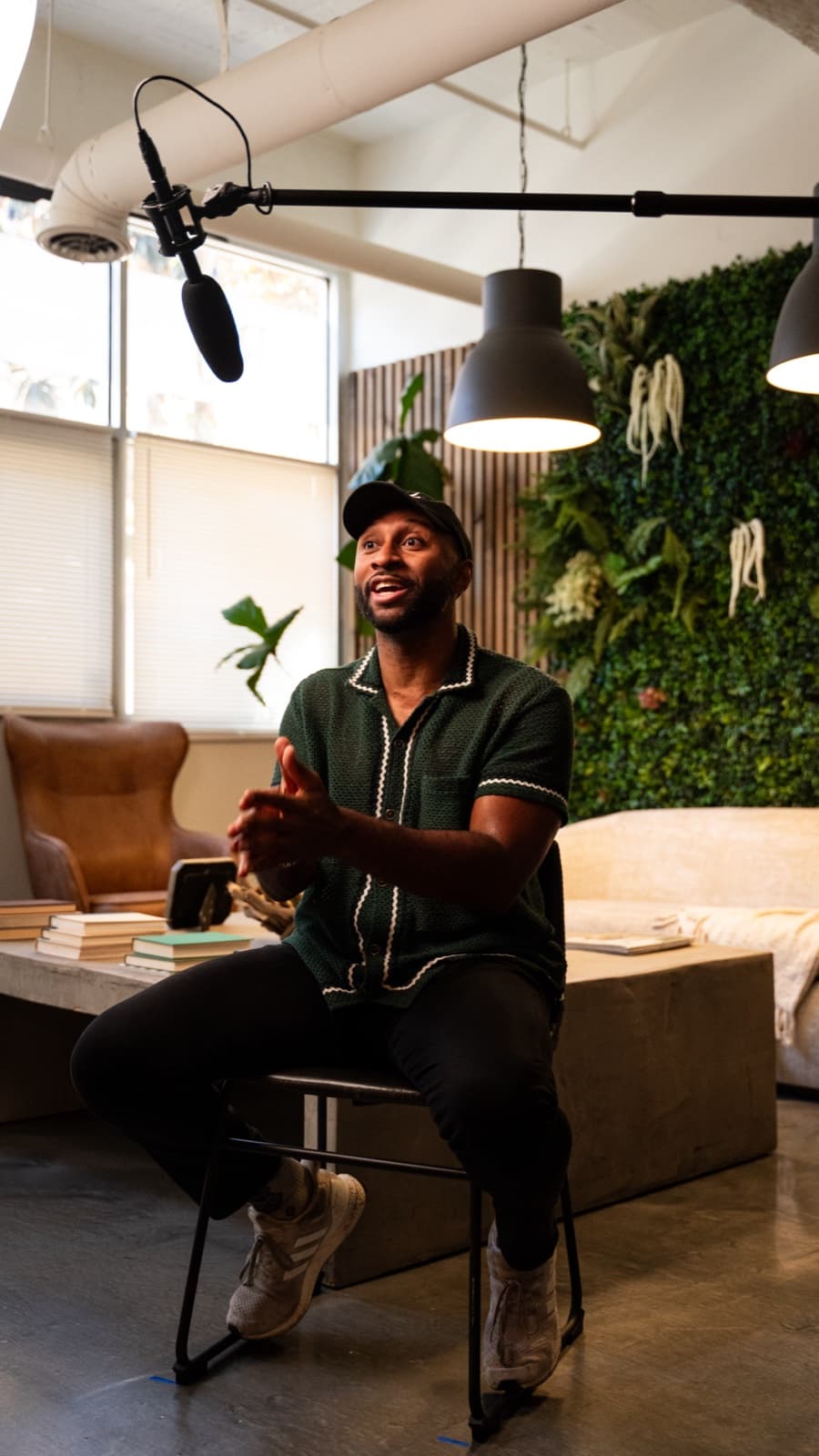 Morgan J. Ingram mid-sentence on a stool in a studio, boom mic overhead and a planted wall behind him.