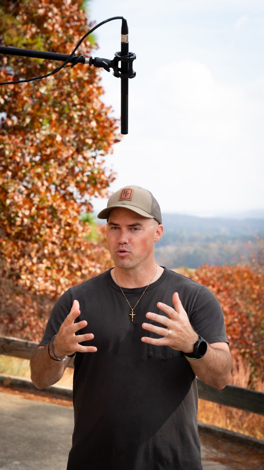Parker Pursell talking to camera outdoors on an overlook, autumn treeline behind him and a boom mic overhead.